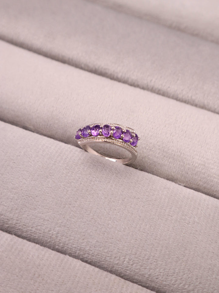 A purple amethyst ring with a gold-colored band, placed on a white surface.