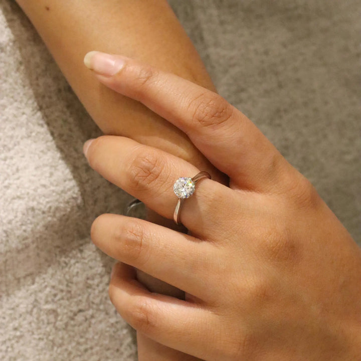 Close-up of a hand wearing a diamond ring on a neutral background