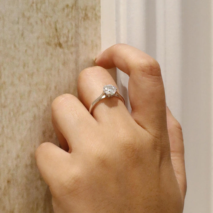 Hand wearing a diamond ring against a neutral background