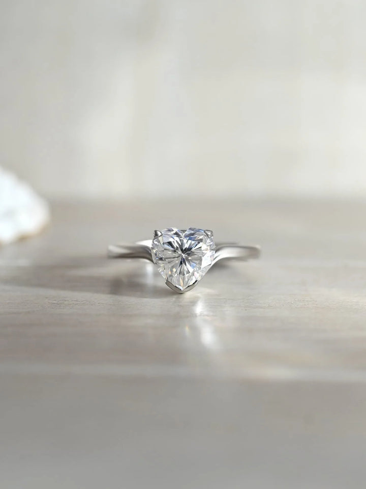A heart-shaped moissanite gemstone set in a 925 sterling silver ring, with rhodium plating and a few small clear stones in the band.
