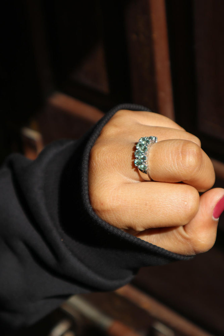 A person's hand displaying a green sapphire ring with a silver band.