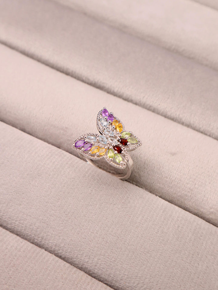 A multicolored gemstone butterfly ring with a silver band, set with amethyst, yellow sapphire, and peridot stones.