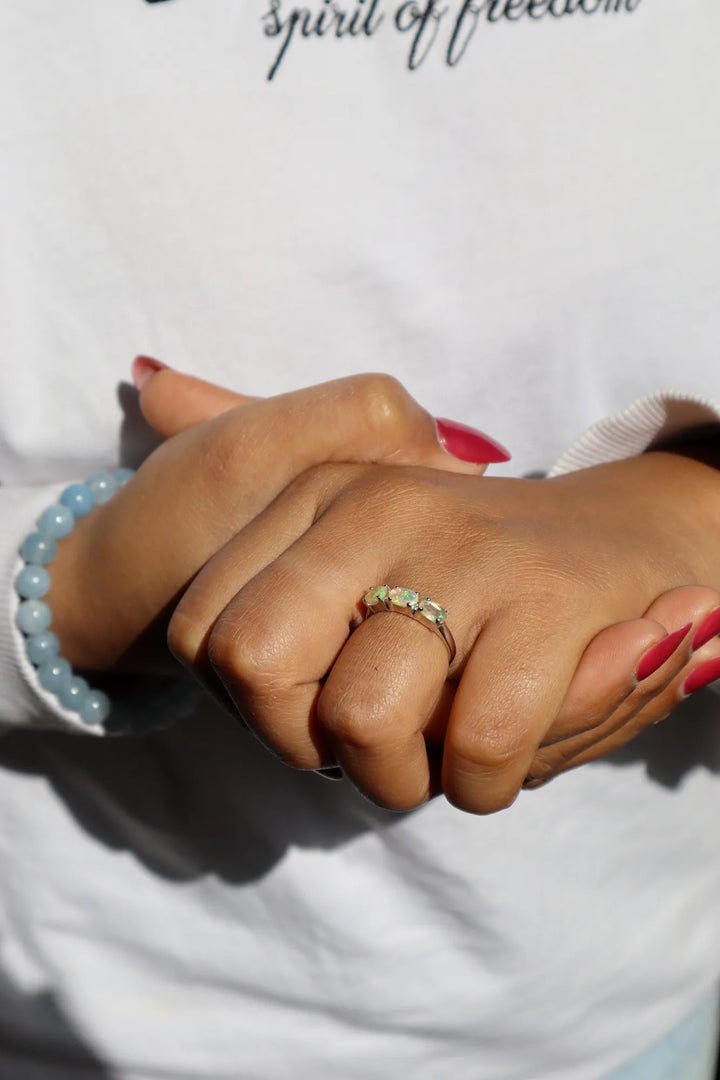 Close-up of hands with a Opal ring and bracelet on a white background with text.