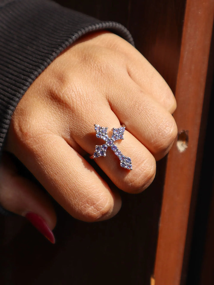 Hand wearing a silver cross-shaped ring with small stones on a dark background