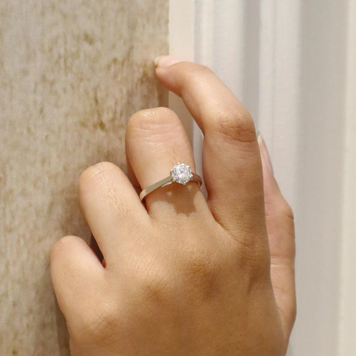 Hand wearing a diamond ring against a neutral background