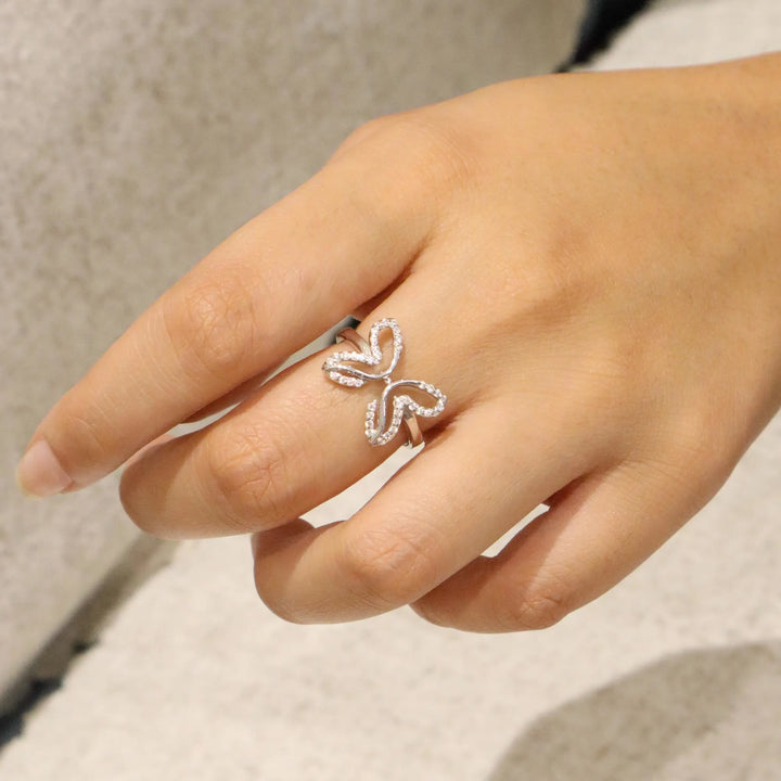 Silver butterfly ring on a person's finger against a neutral background