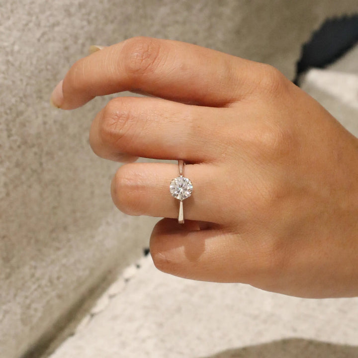 Hand wearing a diamond ring with a neutral background
