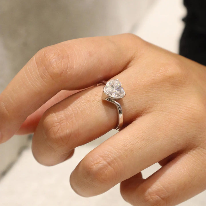 Heart-shaped diamond ring on a finger with a blurred background