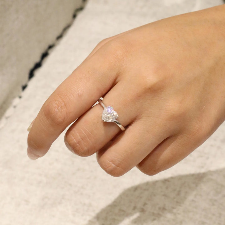 Heart-shaped diamond ring on a finger against a neutral background