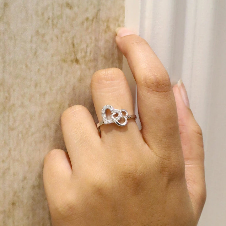Hand wearing a silver ring with a heart design on a neutral background