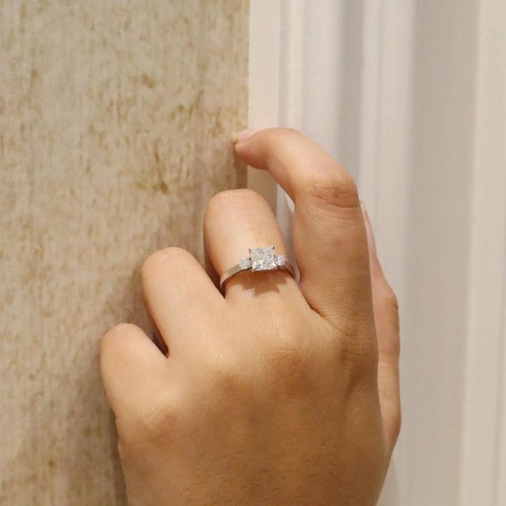 Hand wearing a diamond ring against a neutral background