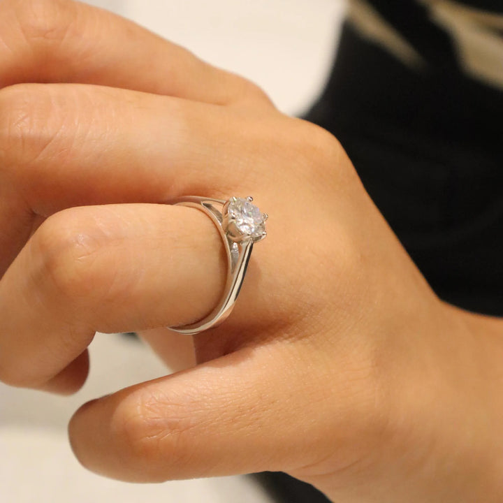 Close-up of a hand wearing a silver ring with a diamond on a neutral background