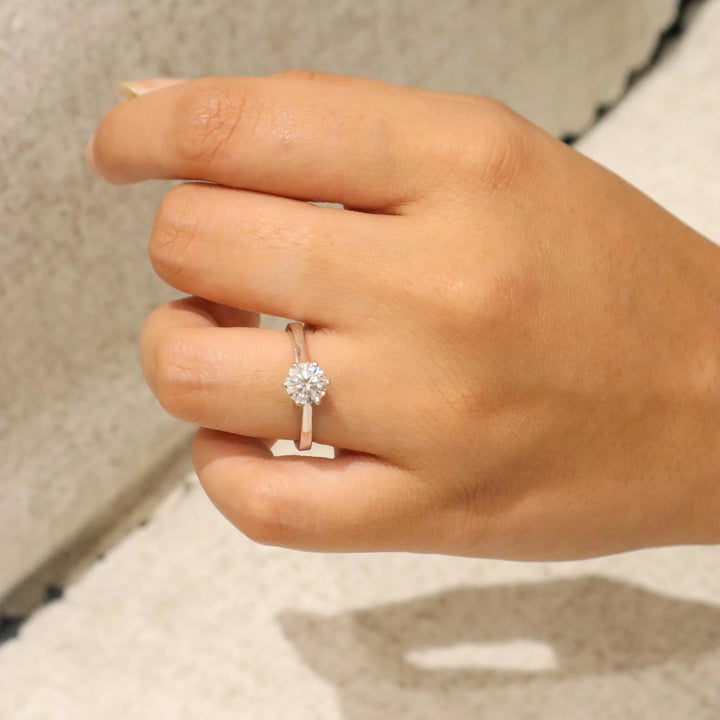 Hand wearing a silver ring with a diamond on a neutral background